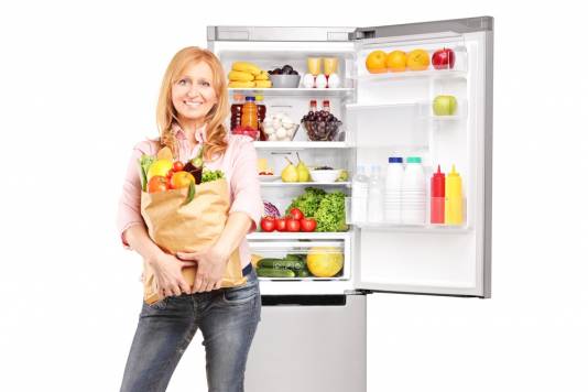 woman with groceries in front of fridge freezer